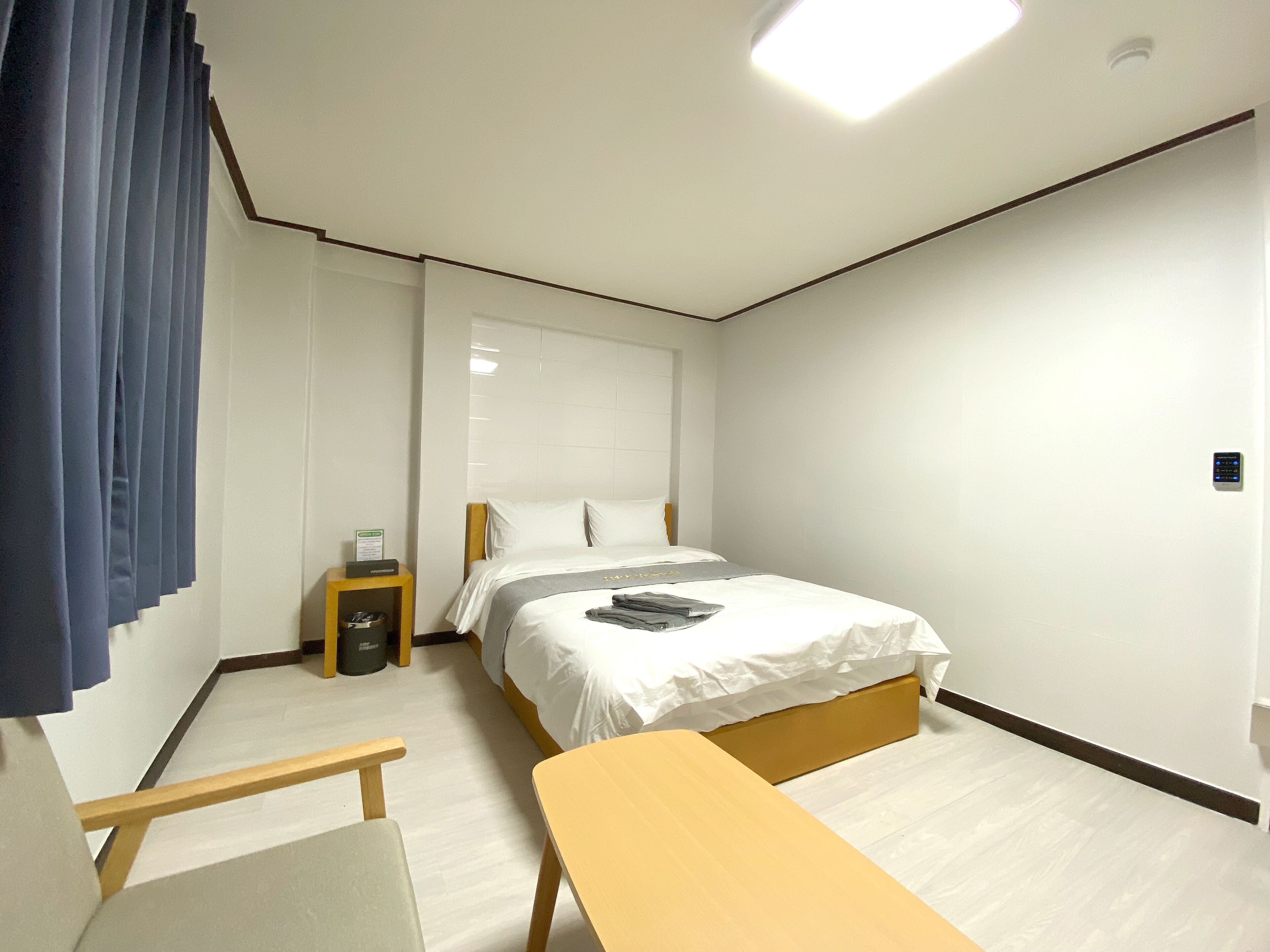 A hotel room with a bed, a bedside table, a chair, a small cabinet, and a window with curtains.