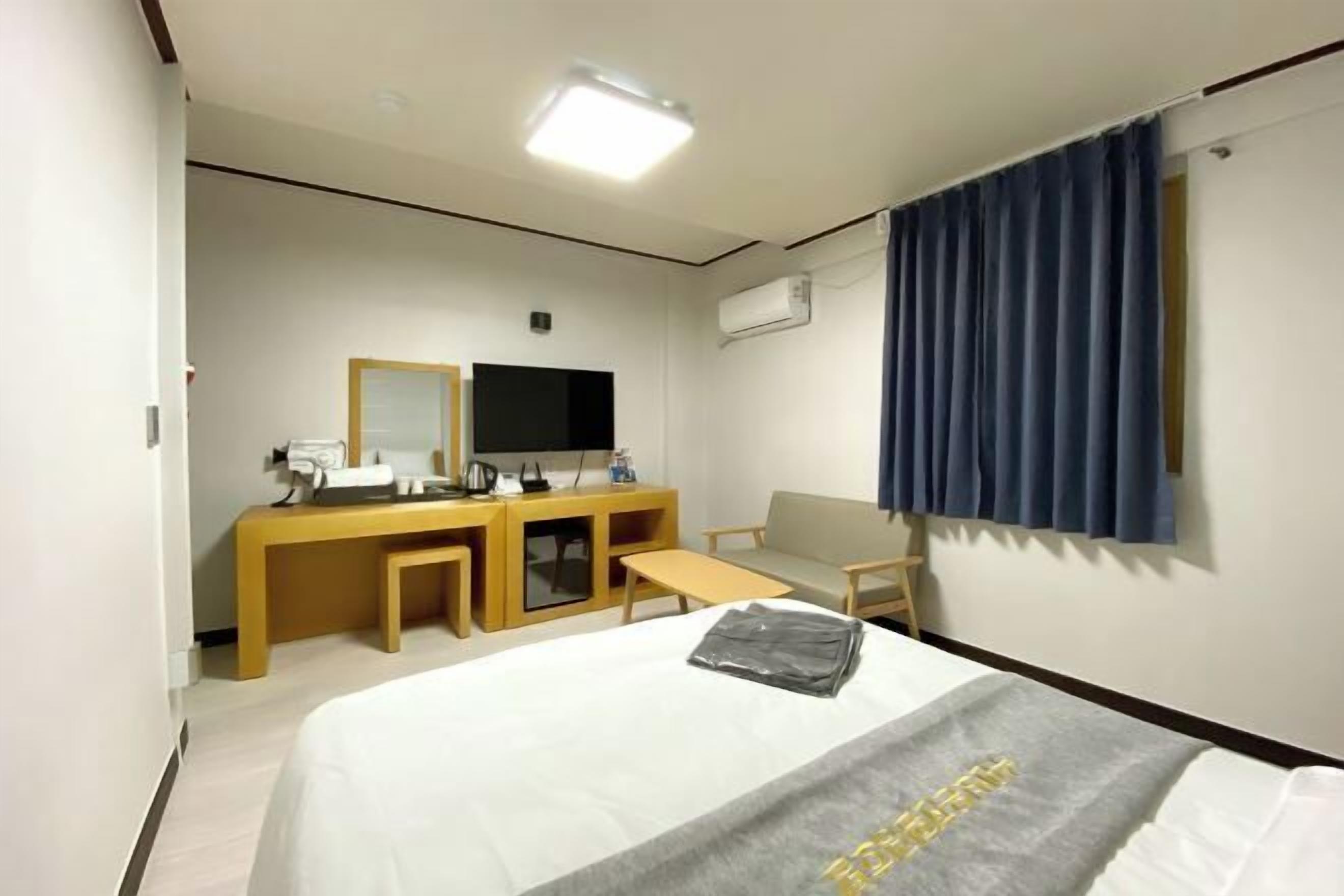 A hotel room with a bed, a desk with a chair, a television, and a window with curtains.