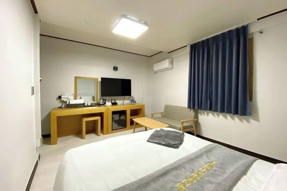 A hotel room with a bed, a desk with a chair, a television, and a window with curtains.