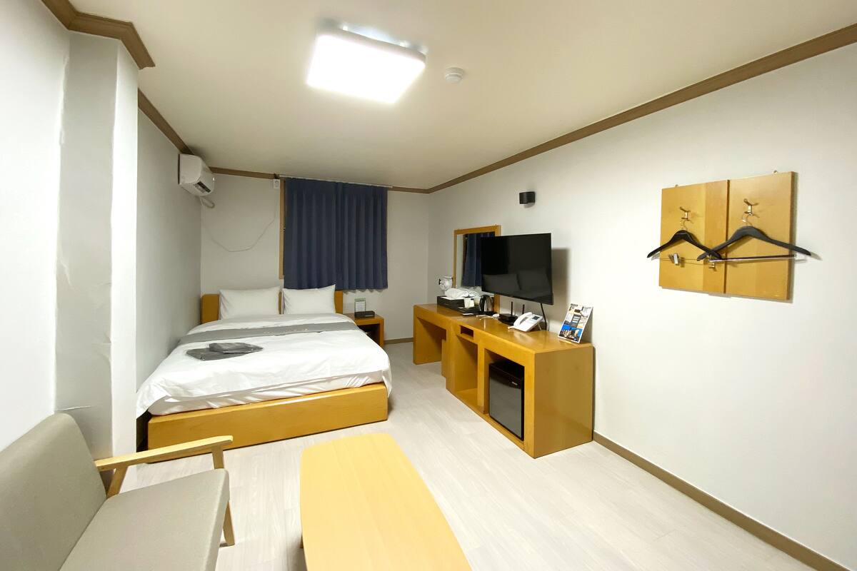 A hotel room with a bed, a desk with a TV, a mirror, and a coat rack.