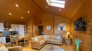 A cozy cabin interior with a wooden interior, a dining area, a sofa, and a fireplace. - Hollybush Lodges (Radstock)