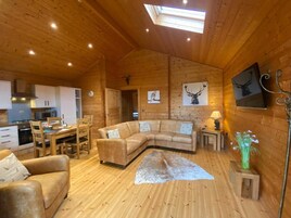 Un acogedor interior de cabaña con paredes y detalles de madera, una zona de comedor, un sof á y una chimenea.