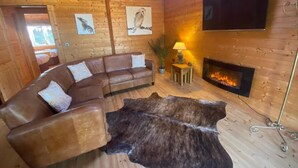 A cozy cabin interior with a leather sofa, a fur rug, a fireplace, and wooden walls. - Hollybush Lodges (Radstock)