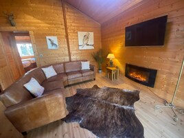 Interior acogedor de una cabaña con un sofá de cuero, un manto de piel, una chimenea y paredes de madera.