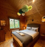 Un dormitorio tipo cabaña de madera con una cama grande, una ventana con vistas y una decoración floral colgante.