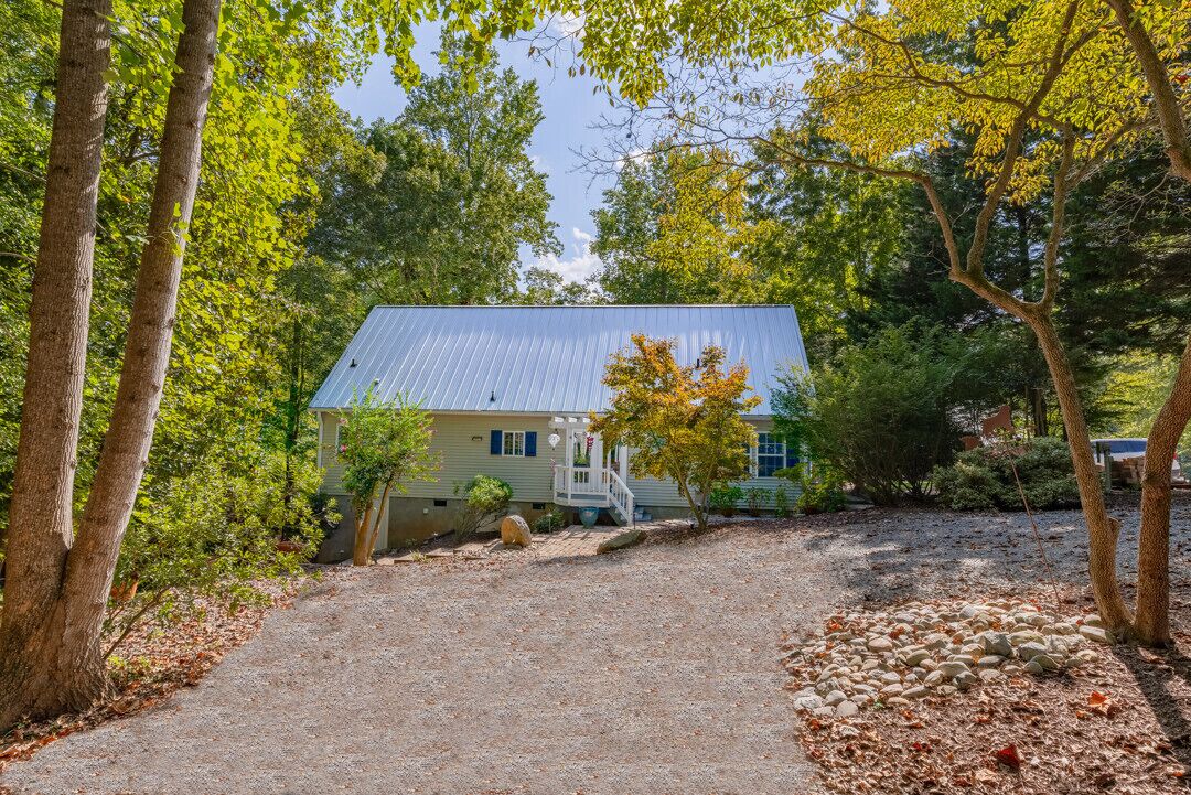 Une maison avec un toit en métal, entourée d’arbres et bordée d’une allée en gravier.