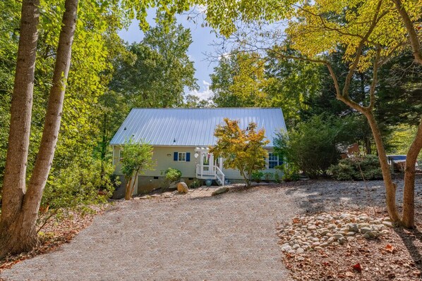 A house with a metal roof, surrounded by trees and a gravel driveway.