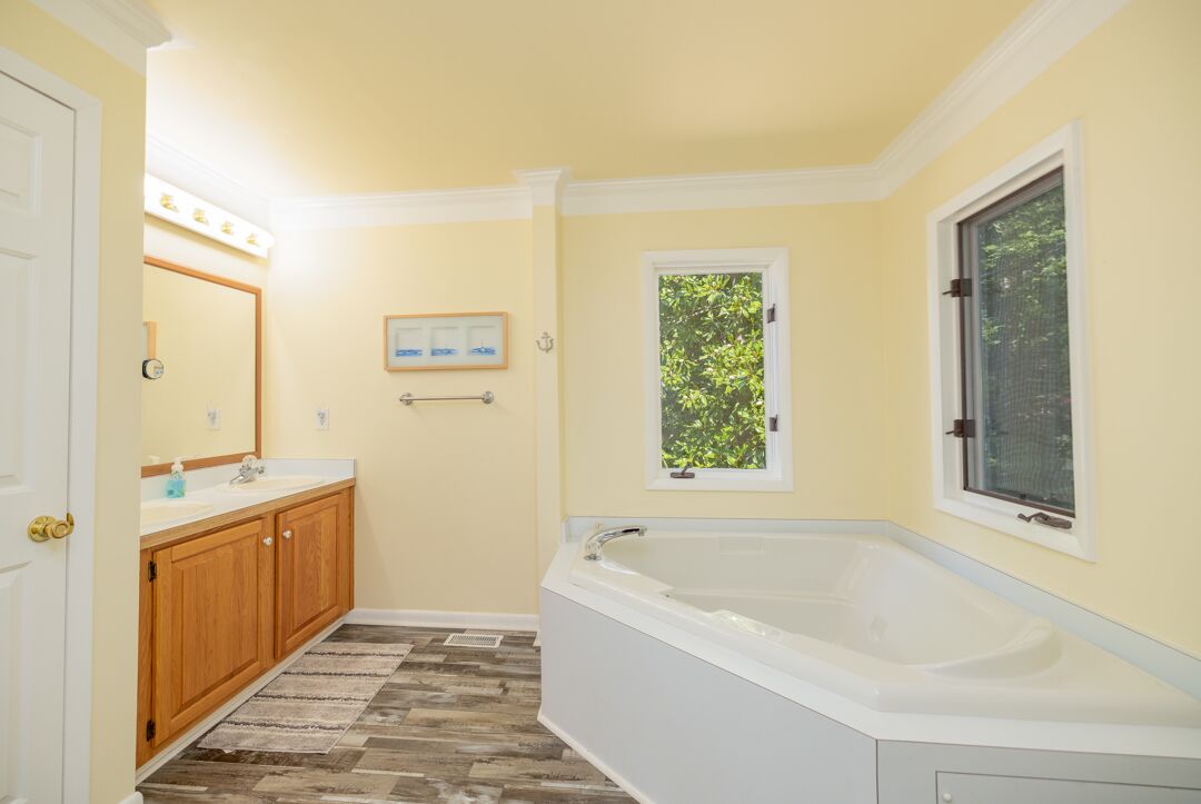 A bathroom with a bathtub, wooden cabinets, a mirror, and a window.