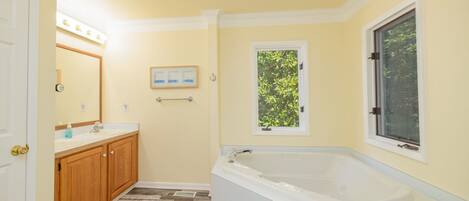 A bathroom with a bathtub, wooden cabinets, a mirror, and a window.