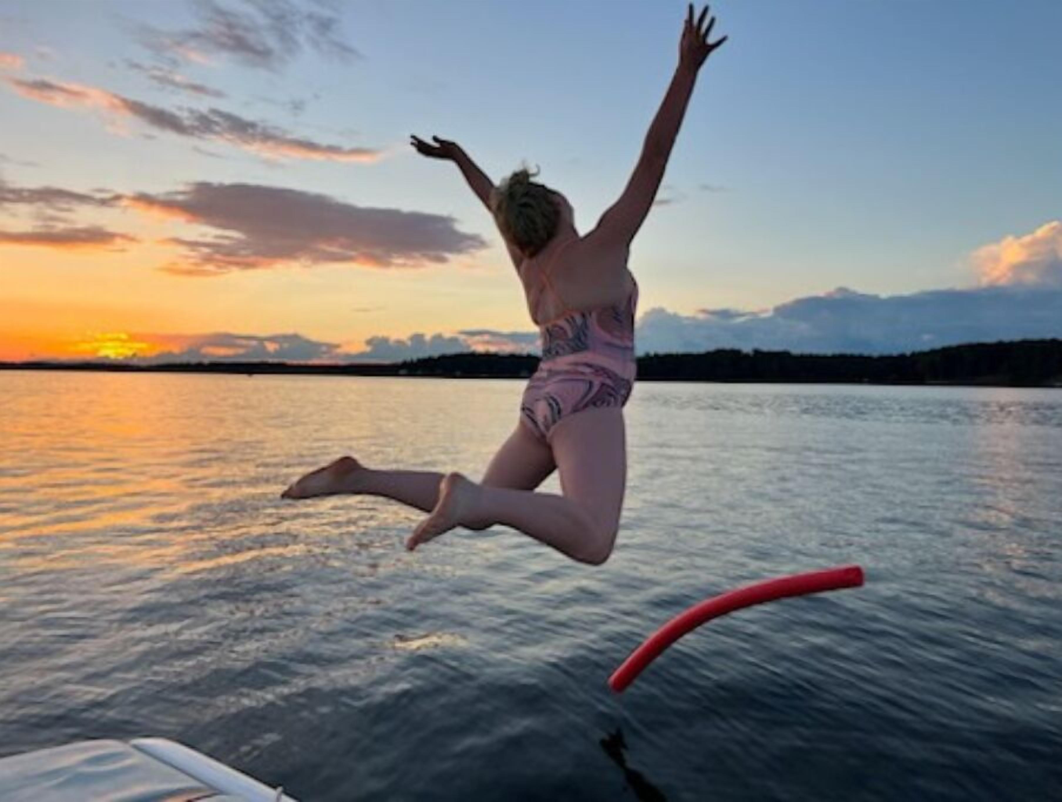 Henkilö hyppää veneestä veteen auringonlaskun aikaan.