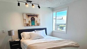 A bedroom with a bed, a nightstand, a lamp, a ceiling light fixture, and a window with a view. - 3 bedroom loft (Wenatchee)