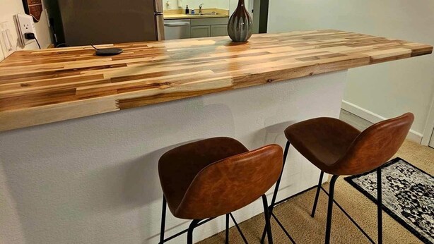 A kitchen with a wooden island, two bar stools, a refrigerator, and a vase with dried flowers. - 3 bedroom loft (Wenatchee)