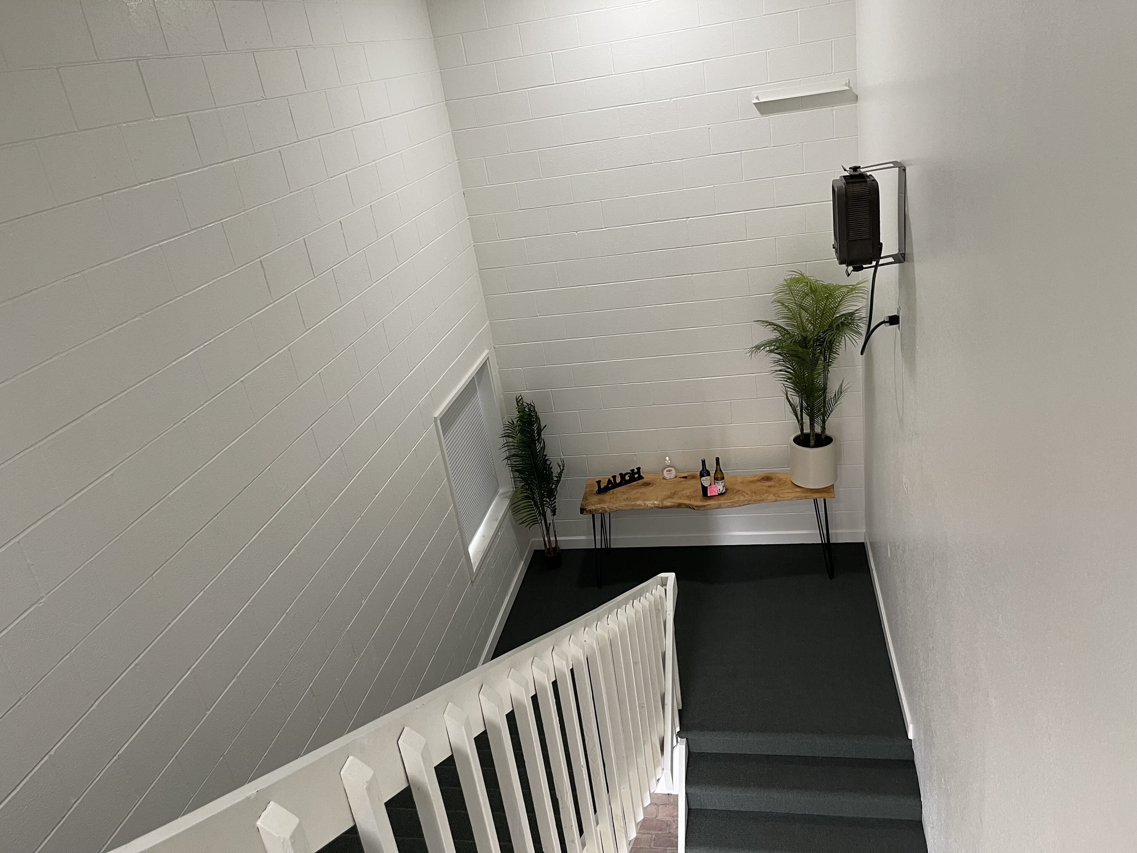 Eine Treppe mit weißen Geländern, ein Holztisch mit einer Zimmerpflanze und eine Wand-Klimaanlage.