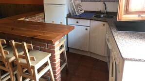 A compact kitchen with a wooden table and chairs, a microwave, a refrigerator, and a sink.