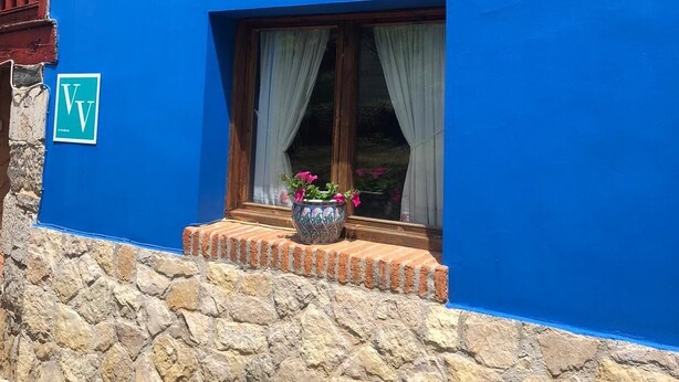 A blue building with a stone foundation, a balcony with wooden railings, and a window with a potted plant.