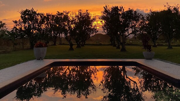 A serene outdoor setting with a reflective pool, trees, and a sunset view. - Family Farm!Wi-Fi,Kiosk,Pool & Mountain Views. (Puerto Samaria)
