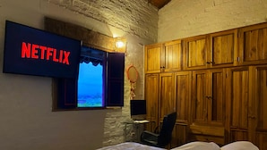 A room with a bed, a TV displaying 'NETFLIX', a window with a view, and wooden cabinets. - Family Farm!Wi-Fi,Kiosk,Pool & Mountain Views. (Puerto Samaria)