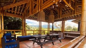 A covered outdoor seating area with bamboo furniture, a picnic table, and a view of the landscape. - Family Farm!Wi-Fi,Kiosk,Pool & Mountain Views. (Puerto Samaria)