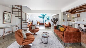 Ein modernes Wohnzimmer mit Wendeltreppe, einer großen Topfpflanze und einer Küchenzeile im Hintergrund.