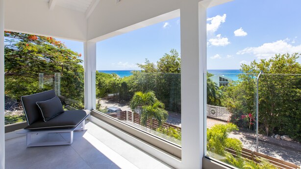 Ein moderner Balkon mit einer schwarzen Couch und einer Glasreling, der einen schönen Blick auf das Meer und üppiges Grün bietet.