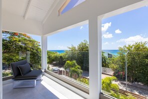 A modern balcony with a black sofa and a glass railing overlooking a scenic view of the sea and lush greenery. - Villa Livity 6 Bed Luxury Sea View boutique villa (Pelican)