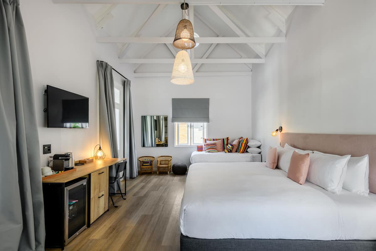 Una habitació d'hotel moderna amb un escriptori de fusta, un llit amb molts coixins, una televisió i una finestra gran.