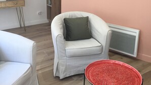 Een woonkamer met een witte fauteuil, een tafel met een rood patroon, een spiegel met gouden lijst en een radiator tegen een roze muur.