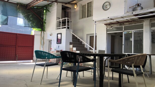 Un espacio al aire libre cubierto con una mesa, sillas, una escalera y un portón rojo.