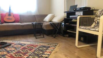 Een woonkamer met een bank, een klein tafeltje, een getextureerd vloerkleed, een gitaar, een stoel en een boekenkast.