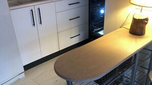 Una cocina con armarios blancos, un fregadero y una encimera. Hay una mesa de madera con una lámpara y dos taburetes.