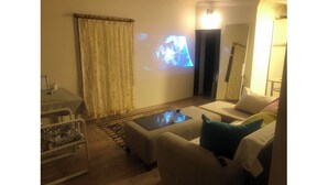Una sala de estar con un sofá, una mesa de centro, un televisor y una mesita de noche con una lámpara.