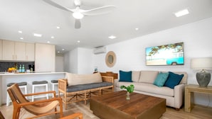 A modern living room with a sofa, coffee table, and chairs, a kitchen area with a bar, and a ceiling fan.