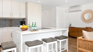 A modern kitchen with white cabinetry, a central island with stools, a coffee machine, and a bowl of fruit.