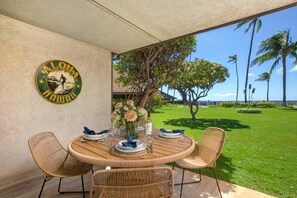 A round wooden table with four wicker chairs, a vase of flowers, and plates set for a meal. A sign on the wall reads "Aloha Hawaii." - Maalaea Surf | Oceanfront 1 BR | Water Front | Car Incl. w/ 6+ Nights | MSR-F2 by KBM (Kihei)