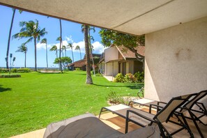 Eine Terrasse mit Sitzgelegenheiten im Freien, einem gepflegten Rasen und Blick auf das Meer und Palmen.