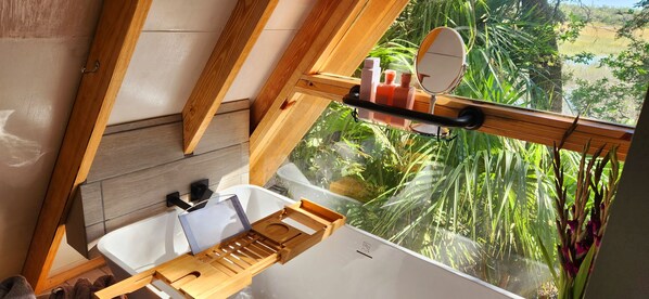 Casa de banho com toucador de madeira, lavatório e janela com vista para vegetação.