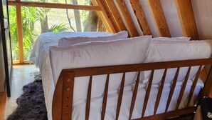 A bedroom with a wooden headboard, white bedding, and a view of greenery outside.