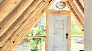 A wooden door with a white panel, a window, and a hanging light fixture in a room with wooden beams.