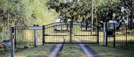 A gated entrance with a metal gate, a pathway leading through, and a signboard.