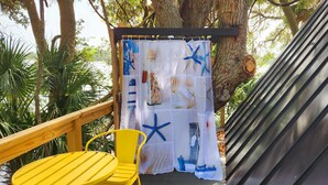 A wooden deck with a yellow chair, a curtain with nautical designs, and a metal structure.