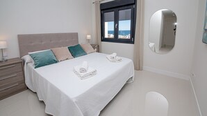 A neatly made bed with a white bedspread and two pillows, a bedside table with a lamp, and a window with a view of the sea. - Paloma Beach apartment 5.1a (Manilva)