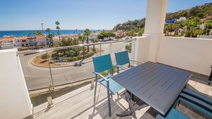 A balcony with a table and chairs overlooking a coastal road with palm trees and buildings. - Paloma Beach apartment 5.1a (Manilva)