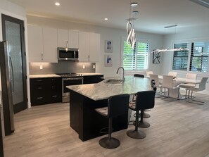 Enjoy cooking in this kitchen with a sleek island, bar stools, microwave, and stainless steel range hood, offering a view of the surrounding greenery.