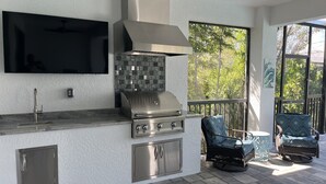A modern outdoor kitchen with a TV, grill, and seating area.