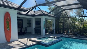 A pool area with a glass-enclosed patio, a surfboard, and outdoor seating.