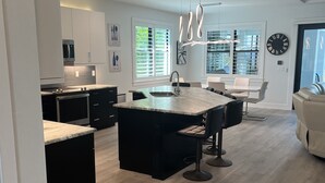 A modern kitchen with a central island, black cabinets, and a dining area with a white table and chairs.