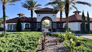 A building with a central archway, surrounded by palm trees and a well-maintained garden. - EPIC VALUE! Private Pool Oasis! Water Slide! Close 2 Disney! 5488 (Davenport)