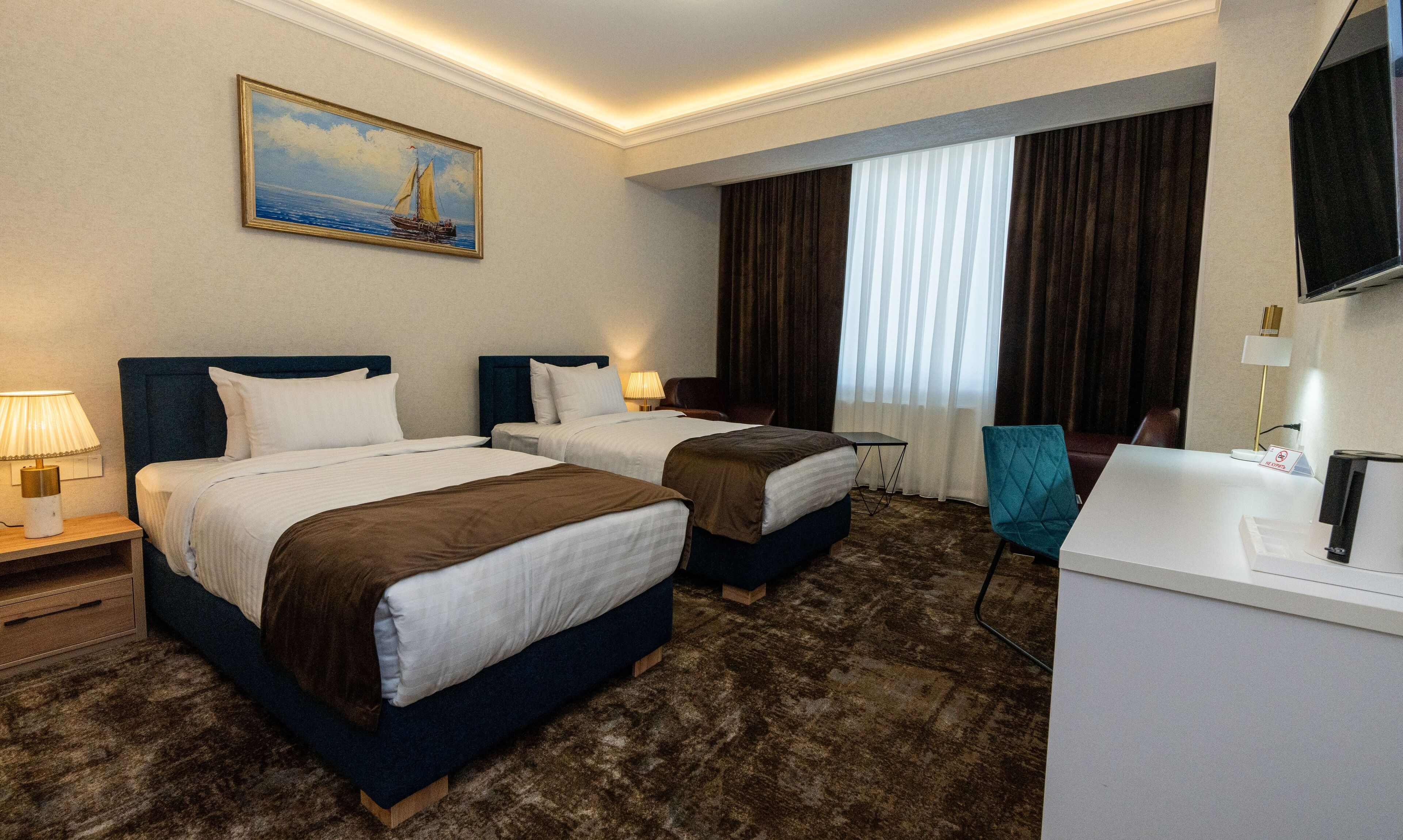 A hotel room with two beds, a desk, a chair, a TV, a painting, and a window with curtains.