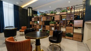 A modern interior with a round table, leather chairs, a dark-colored sofa, and a wooden shelving unit with plants and decorative items. - Garnet Mir Hotel (Tashkent)