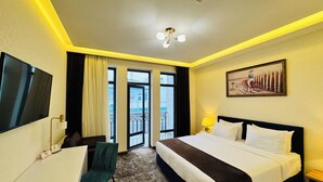 A hotel room with a bed, desk, chair, and a painting on the wall. - Garnet Mir Hotel (Tashkent)